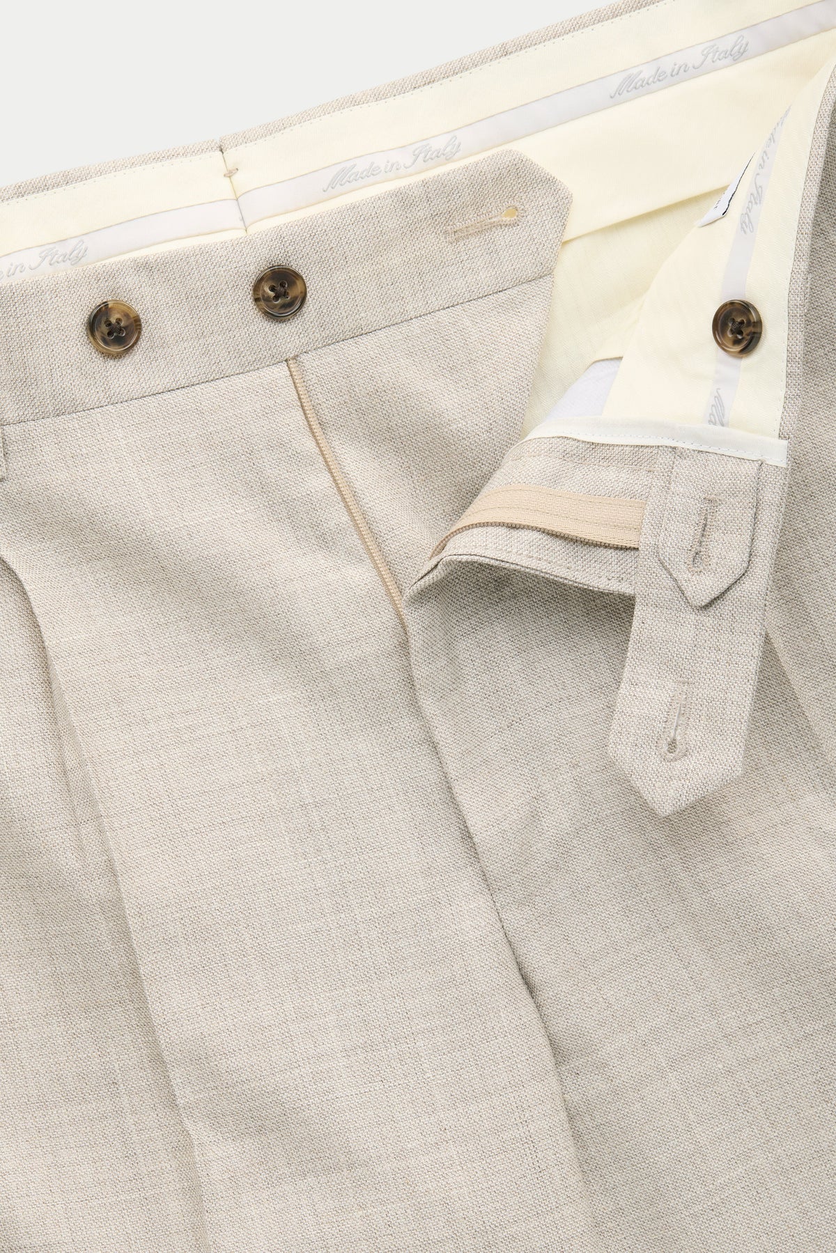 Close-up of light-colored tailored trousers showing the interior waistband, button closures, and front pleats